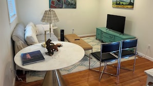 A modern living room with a sofa, a coffee table, a lamp, a TV on a teal cabinet, and artwork on the walls.