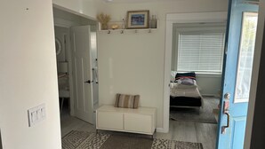 A bedroom with a bed, a bedside table, a window with blinds, and a door.