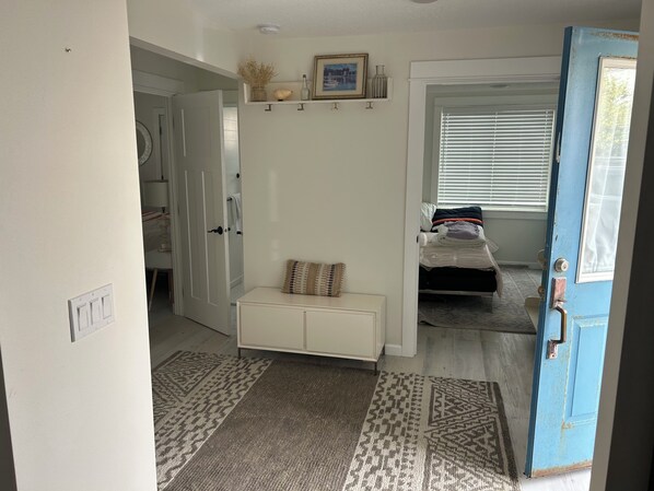 A bedroom with a bed, a bedside table, a window with blinds, and a door.