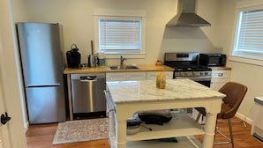 A compact kitchen with a stainless steel refrigerator, a dishwasher, a stove, and a microwave. There is a marble countertop with a chair and a small table.