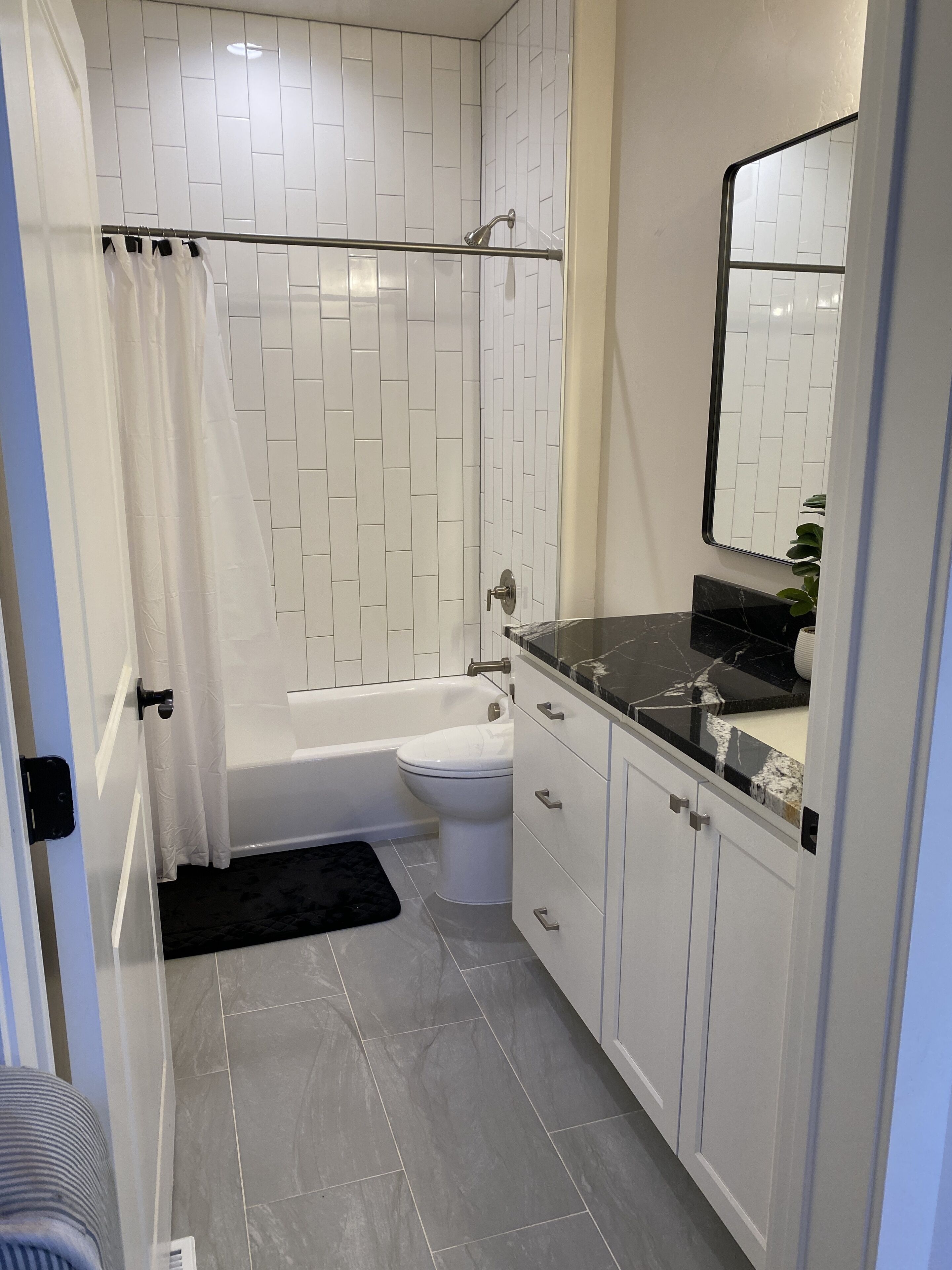 Un bagno moderno con pareti piastrellate di bianco, un lavabo in marmo nero e una vasca da bagno bianca.