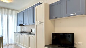 A modern kitchen with grey cabinets, a black TV, and a microwave. - Villa Emy 11 Fronte Mare - Carraro Immobiliare Jesolo (Lido di Jesolo)