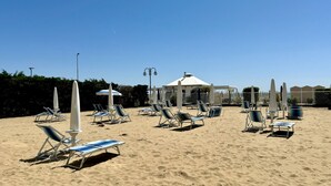 A beach with rows of sun loungers and umbrellas, a gazebo, and a fence. - Villa Emy 11 Fronte Mare - Carraro Immobiliare Jesolo (Lido di Jesolo)