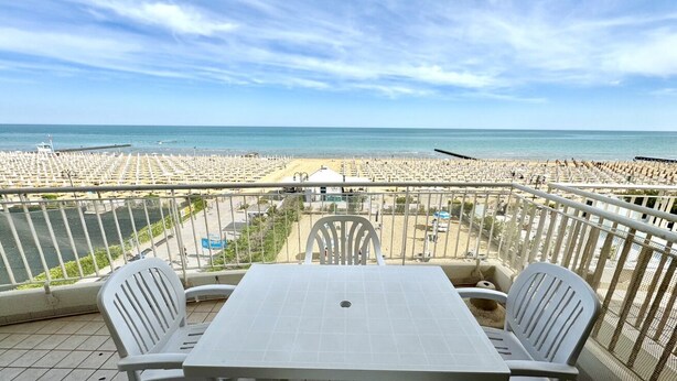 A balcony with a table and chairs overlooking a beach with rows of sunbeds. - Villa Emy 11 Fronte Mare - Carraro Immobiliare Jesolo (Lido di Jesolo)