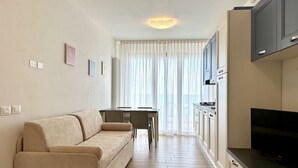 A modern living room with a sofa, a dining table, and a kitchen area with cabinets and a TV. - Villa Emy 11 Fronte Mare - Carraro Immobiliare Jesolo (Lido di Jesolo)