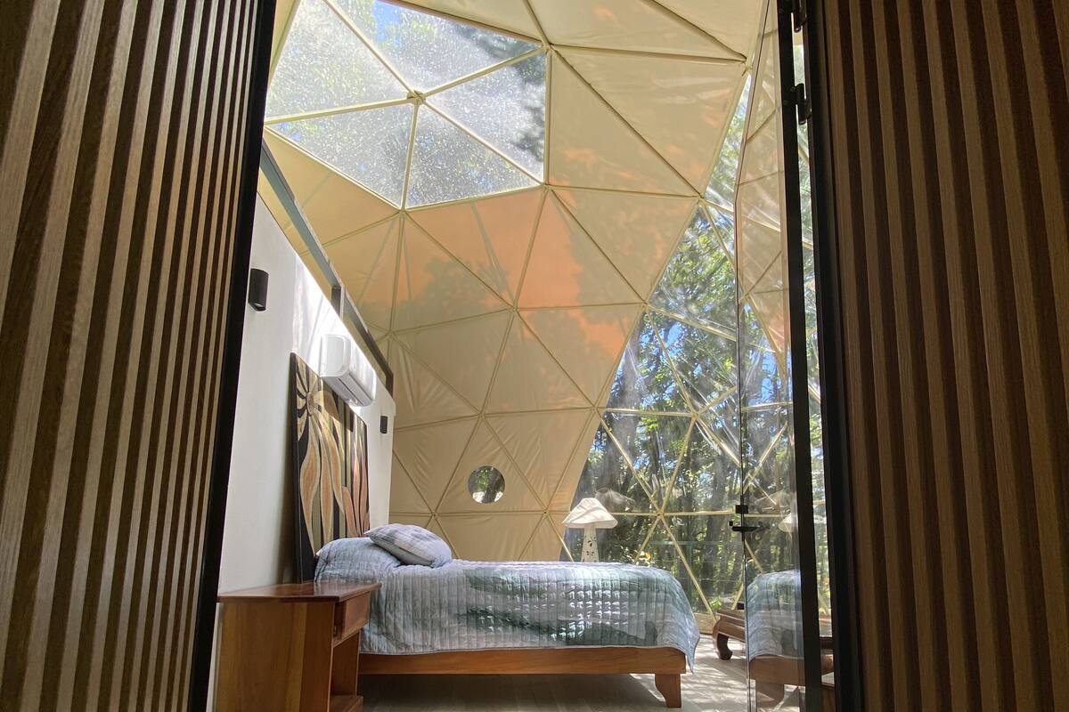 A modern bedroom with a geometric ceiling structure, a wooden bed, and a nightstand.