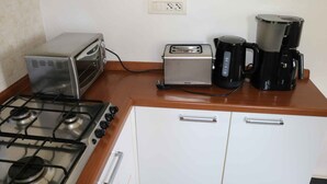 Cucina con piano cottura a gas, tostapane, macchina del caffè e mobiletto bianco.