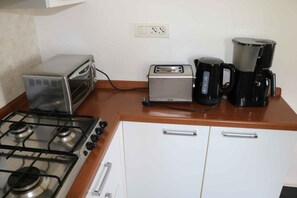 A kitchen with a gas stove, a toaster, a coffee maker, and a white cabinet.