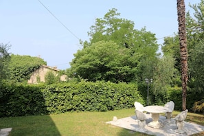 A garden with a stone table and chairs, a palm tree, and a hedge.