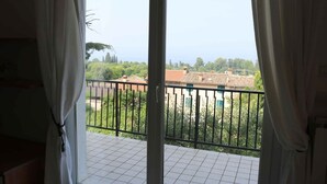 Un balcone con vista su una zona residenziale, un pavimento piastrellato e tende parzialmente aperte.