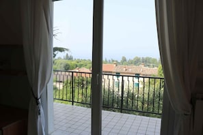 A balcony with a view of a residential area, a tiled floor, and curtains partially drawn.