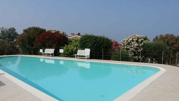 Una piscina con due poltrone bianche, circondata da una recinzione e diverse piante fiorite.