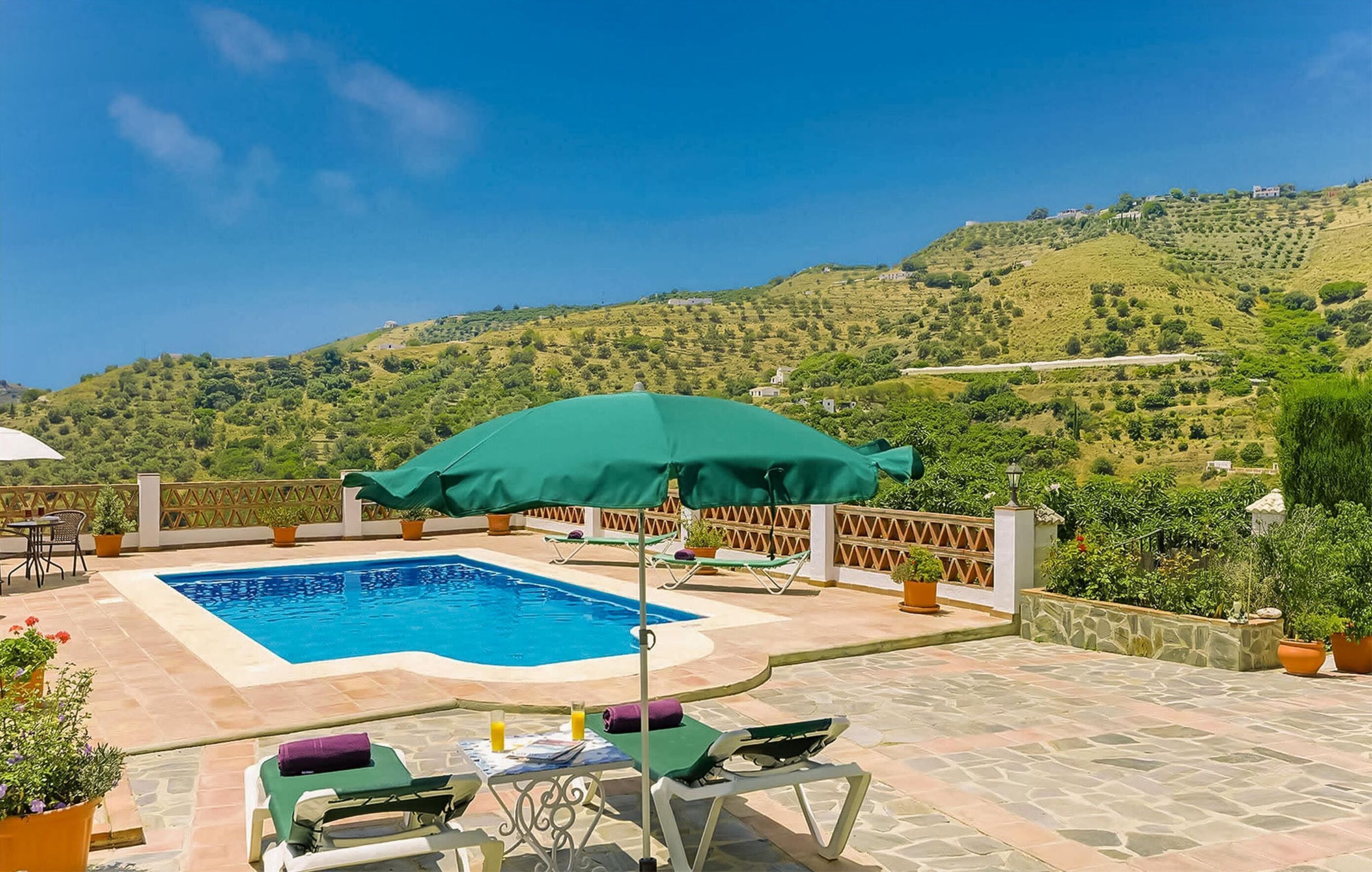 A pool area with lounge chairs and umbrellas, surrounded by stone flooring and potted plants.