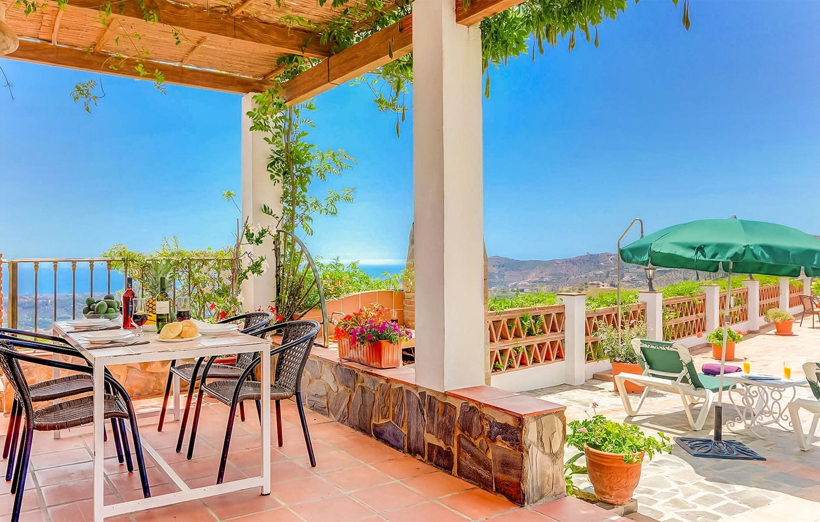 An outdoor patio with a table set for dining, surrounded by potted plants and a view of the sea.