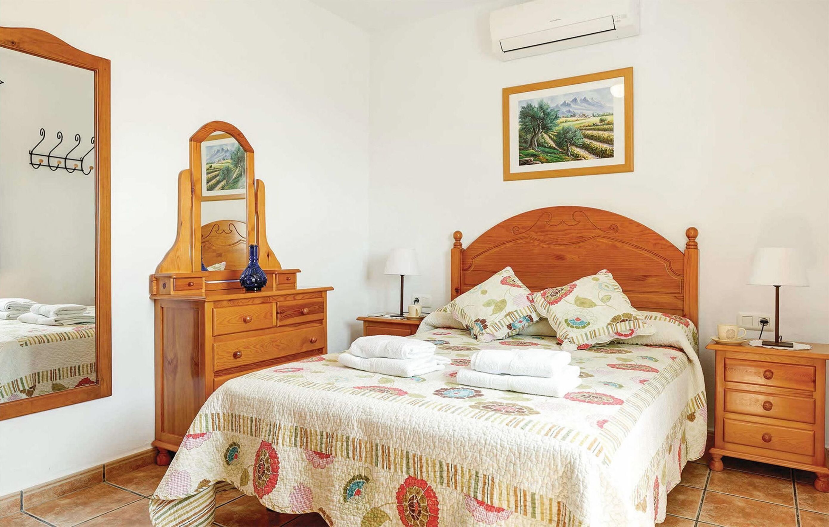 A bedroom with a wooden bed, a dresser with a mirror, a nightstand with a lamp, and a wall-mounted air conditioner.