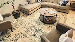 A living room with a sectional sofa, a coffee table, a potted plant, and a wall clock. - 30 Sec. to Beach, Sun, Sand & Waves  &  a Family & Pet Friendly Fenced Backyard (Carolina Beach)
