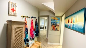 A hallway with a wooden cabinet, colorful towels, a painting of sailboats, and a 'No Lifeguard on Duty' sign. - 30 Sec. to Beach, Sun, Sand & Waves  &  a Family & Pet Friendly Fenced Backyard (Carolina Beach)