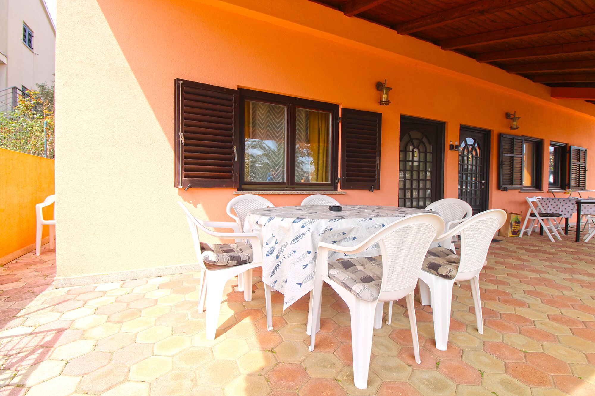 Une terrasse extérieure avec une table et des chaises, un sol carrelé et un bâtiment aux murs et volets orange.
