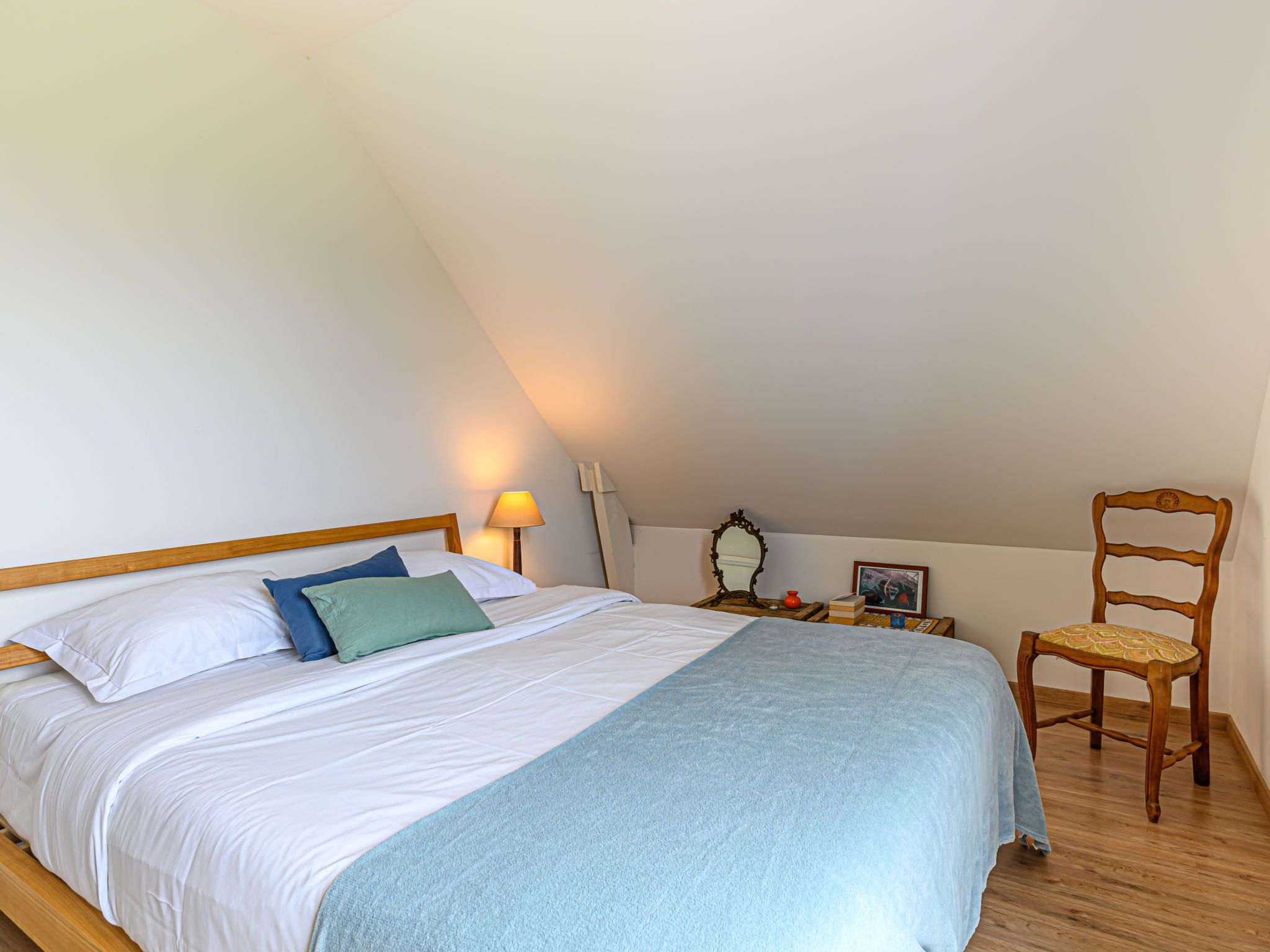 A bedroom with a bed, a chair, a nightstand, and a lamp.