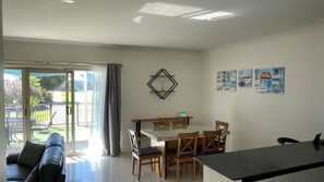 A modern living room with a sofa, a dining table with chairs, a sliding glass door leading to a patio, and wall art.