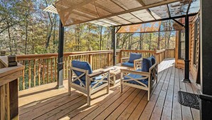Una terraza de madera con mobiliario exterior y una pérgola que proporciona sombra.