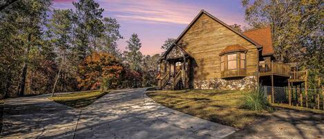 A wooden cabin with a stone foundation, a covered porch, and a fenced deck.