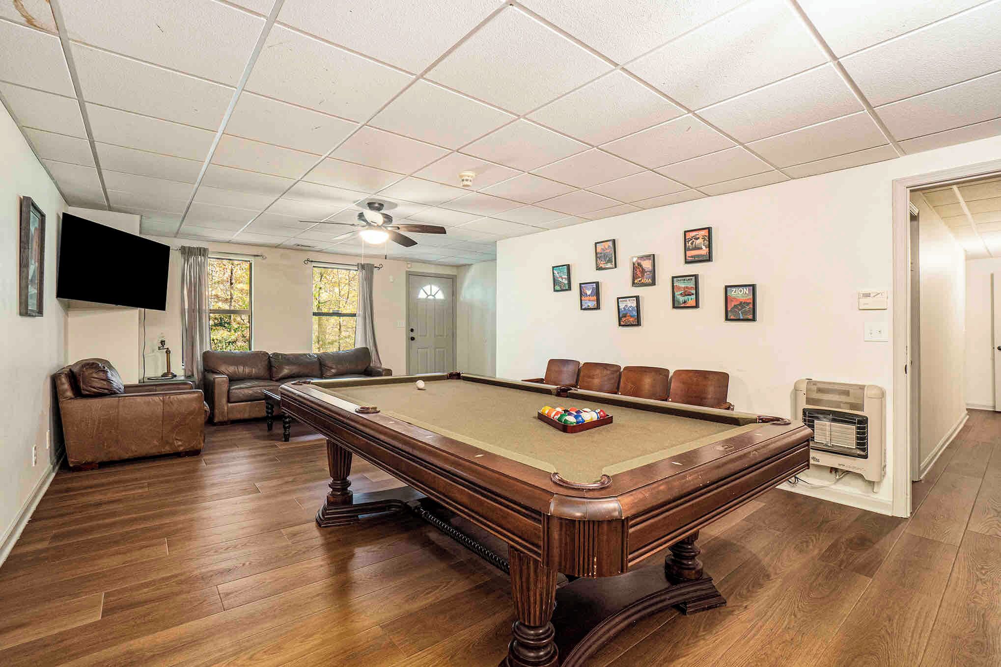 A pool table in a room with a ceiling fan, a sofa, and a television.