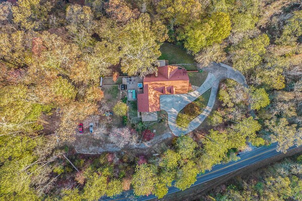 Vista aérea de una casa rodeada de árboles, con un camino de entrada curvo.