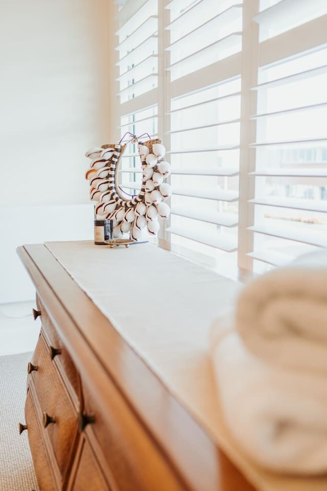 A wooden dresser with drawers, a mirror with a decorative frame, and a window with blinds.