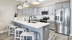 A modern kitchen with white cabinets, stainless steel appliances, and pendant lighting.