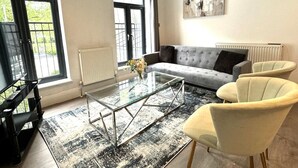 Un salon avec un canapé gris, deux fauteuils, une table basse en verre et un meuble TV noir.