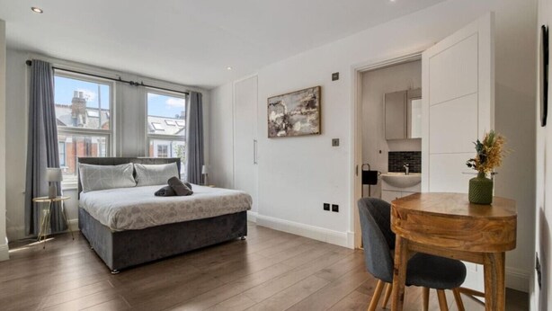Une chambre à coucher moderne, dotée d’un grand lit, d’une table à manger et offrant une vue sur la ville par la fenêtre.