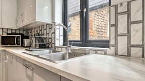 Une cuisine moderne dotée d’appareils électroménagers en acier inoxydable, d’un évier à deux bacs et d’une fenêtre donnant sur un bâtiment en briques.