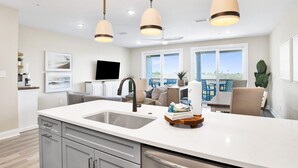 A modern kitchen with a large island, pendant lights, and a view to the outdoors. - Serenity Sunrise: Gulf Shores Luxury Condo (Gulf Shores)
