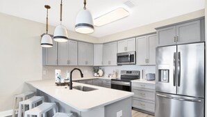 A modern kitchen with grey cabinets, stainless steel appliances, and a central island with bar stools. - Serenity Sunrise: Gulf Shores Luxury Condo (Gulf Shores)