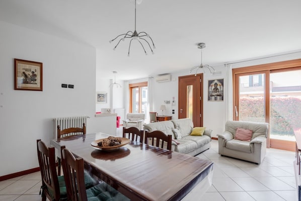 A modern living room with a dining table, chairs, a sofa, and a window with a view.