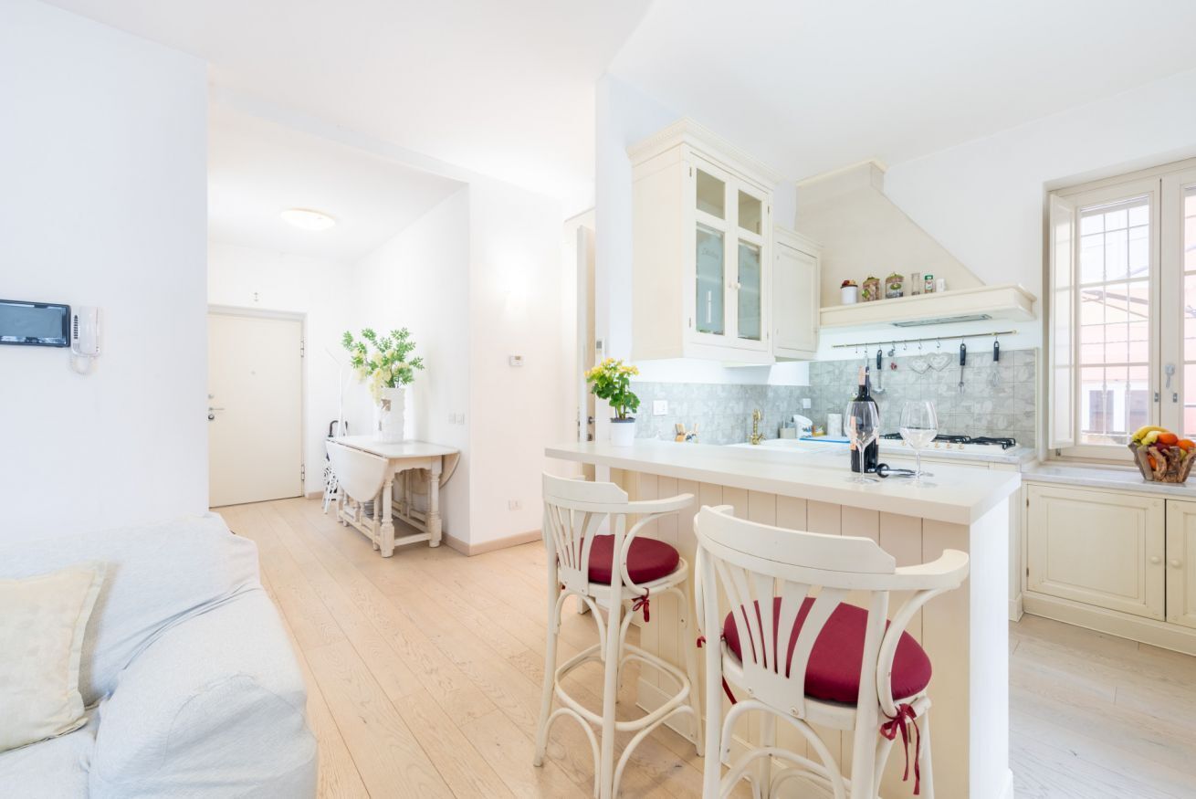 Una cucina moderna con mobili bianchi, un'isola centrale e sgabelli da bar.