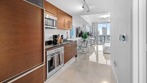 A modern kitchen with wooden cabinets, stainless steel appliances, and a dining area with a view of the cityscape. - Studio in Miami/Brickell Business District-ICON Residences (Miami)
