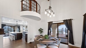 A spacious dining area with a round table, wooden chairs, and a central island. A chandelier hangs above, and the room has large windows with curtains. - Beautiful Fallbrook Estate Ideal for Weddings and Events (Fallbrook)