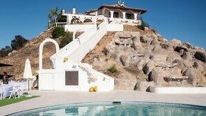 A pool with a circular design, a white building with a staircase, and a rocky hillside. - Beautiful Fallbrook Estate Ideal for Weddings and Events (Fallbrook)