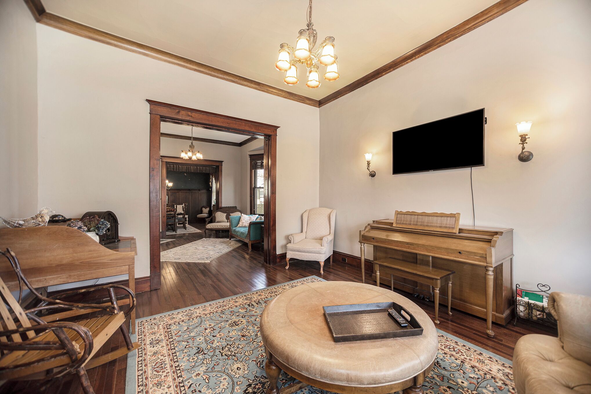 A living room with a wooden coffee table, a piano, a television, and a chandelier.