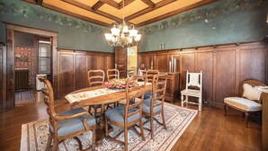 A dining room with a wooden table and chairs, a chandelier, and a patterned rug.