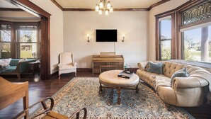 A living room with a large round coffee table, a beige sofa, a wooden piano, and a chandelier.