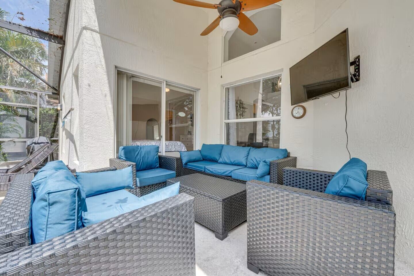 An outdoor patio area with wicker furniture, a ceiling fan, and large windows.