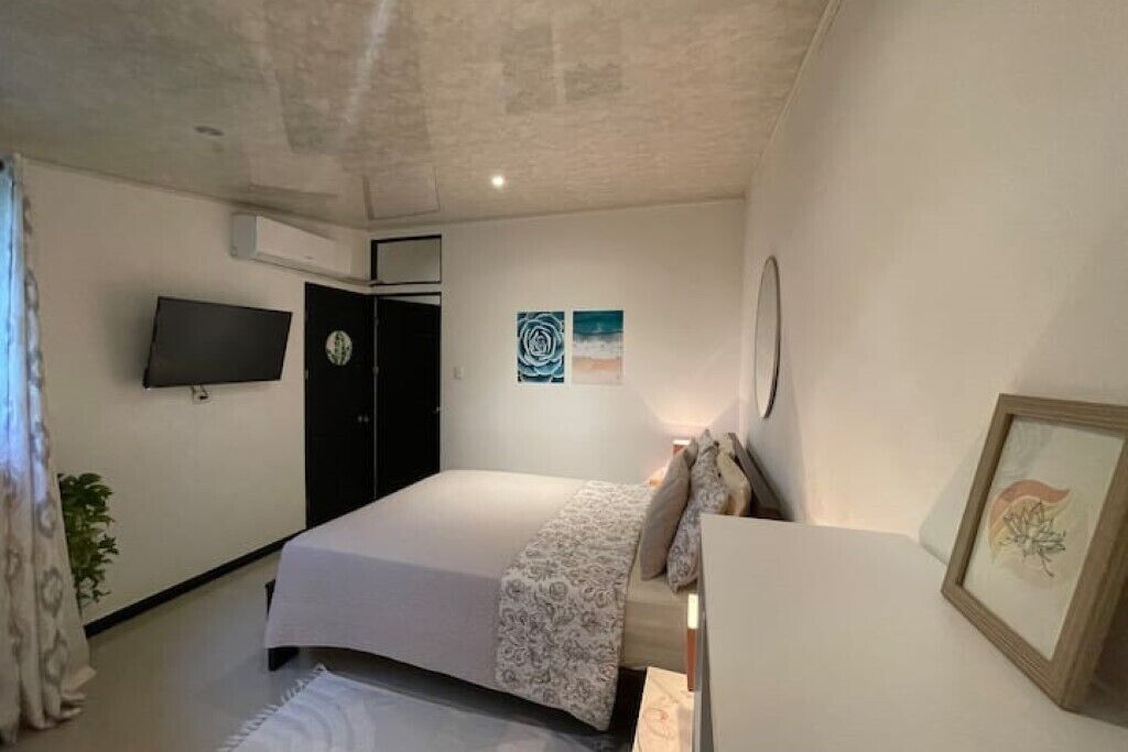 Ein Schlafzimmer mit einem Bett, einem an der Wand montierten Fernseher, einer Tür und einem gerahmten Bild.