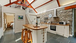 A spacious kitchen with a stone wall, wooden beams, and a high ceiling. - Penpedwast Upper Barn, Newport (Eglwyswrw)