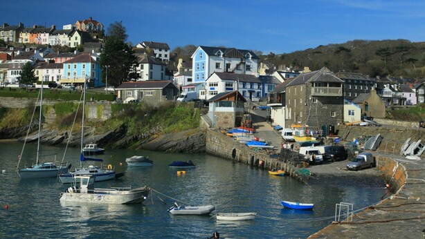 A coastal town with a harbor filled with boats, houses with colorful facades, and a prominent blue building.