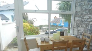 A dining area with a wooden table and chairs, a window with a view of houses and a car, and a mat at the door.
