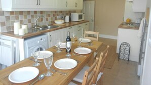 A modern kitchen with white cabinets, a wooden dining table set for four, and a small island with a microwave.
