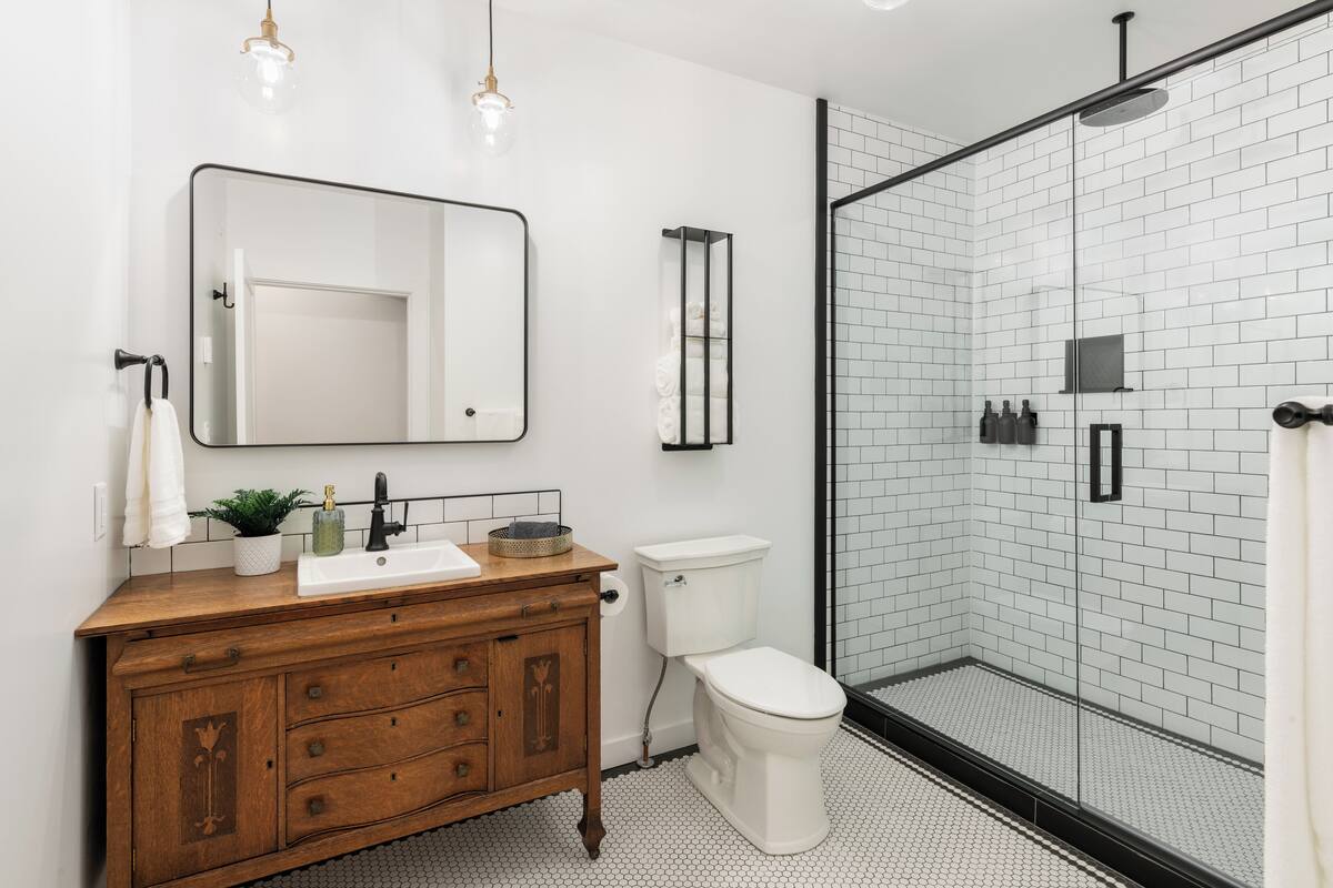 A modern bathroom with a wooden vanity, a white toilet, and a glass shower enclosure.